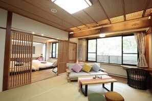 Una habitación de estilo japonés tradicional con suelo de tatami, una mesa baja, un sofá con cojines y un puertas correderas.