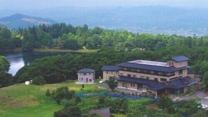 A large, multi-story building with a flat roof, surrounded by lush greenery and a lake. - Zao Onsen Kinosato (Yamagata)