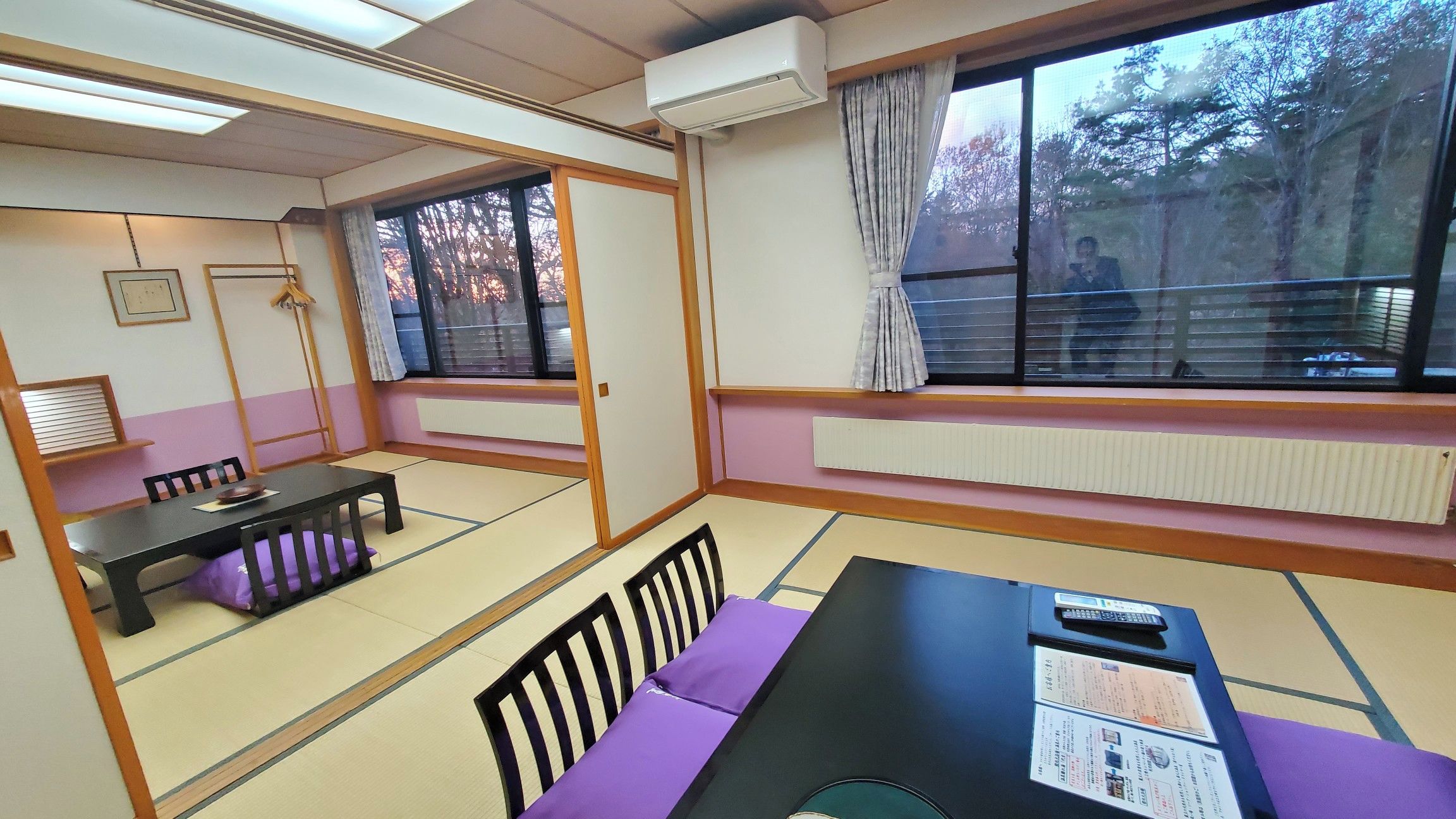 A traditional tatami room with a low table and chairs, a window with a view of trees, and a radiator.