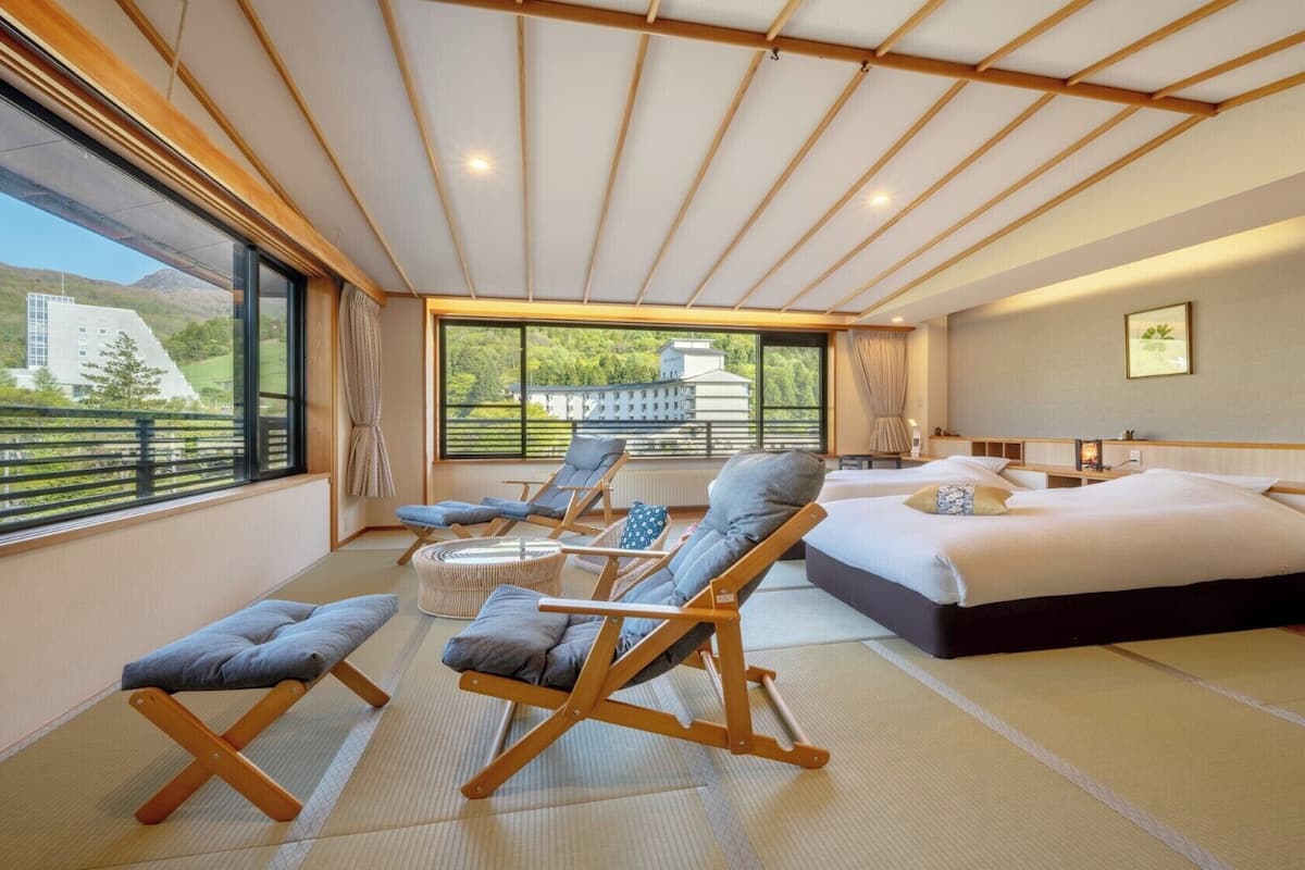 Een moderne hotelkamer met een groot bed, twee fauteuils, een bijzettafeltje en uitzicht op het landschap.