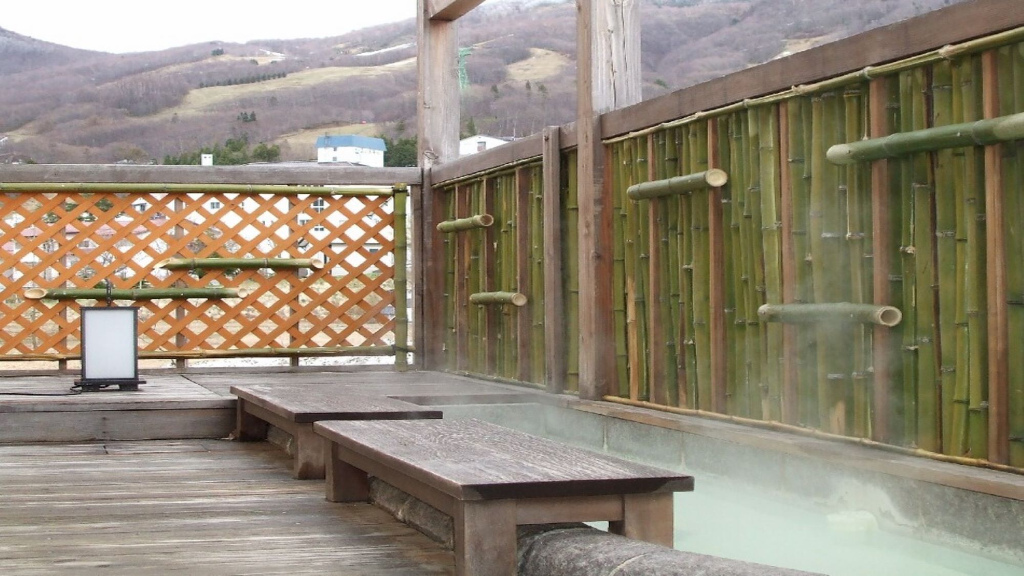 Um deck de madeira com bancos, cerca de madeira e parede de bambu.