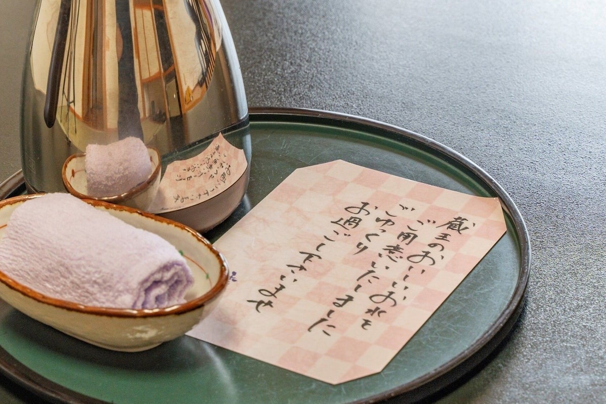 Een theepot, een kom met een handdoek en een stuk papier met Japanse tekst op een dienblad.