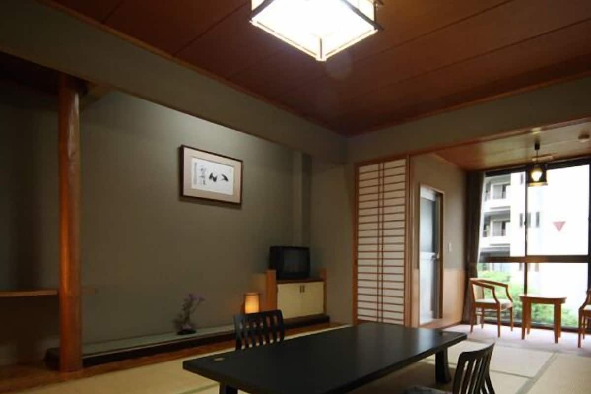 A traditional Japanese room with tatami flooring, a low table, chairs, a television, and sliding doors.