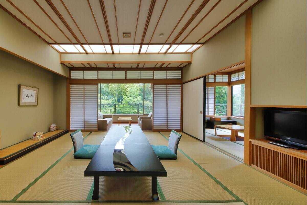 A traditional Japanese room with tatami flooring, a low table, seating, and a TV.