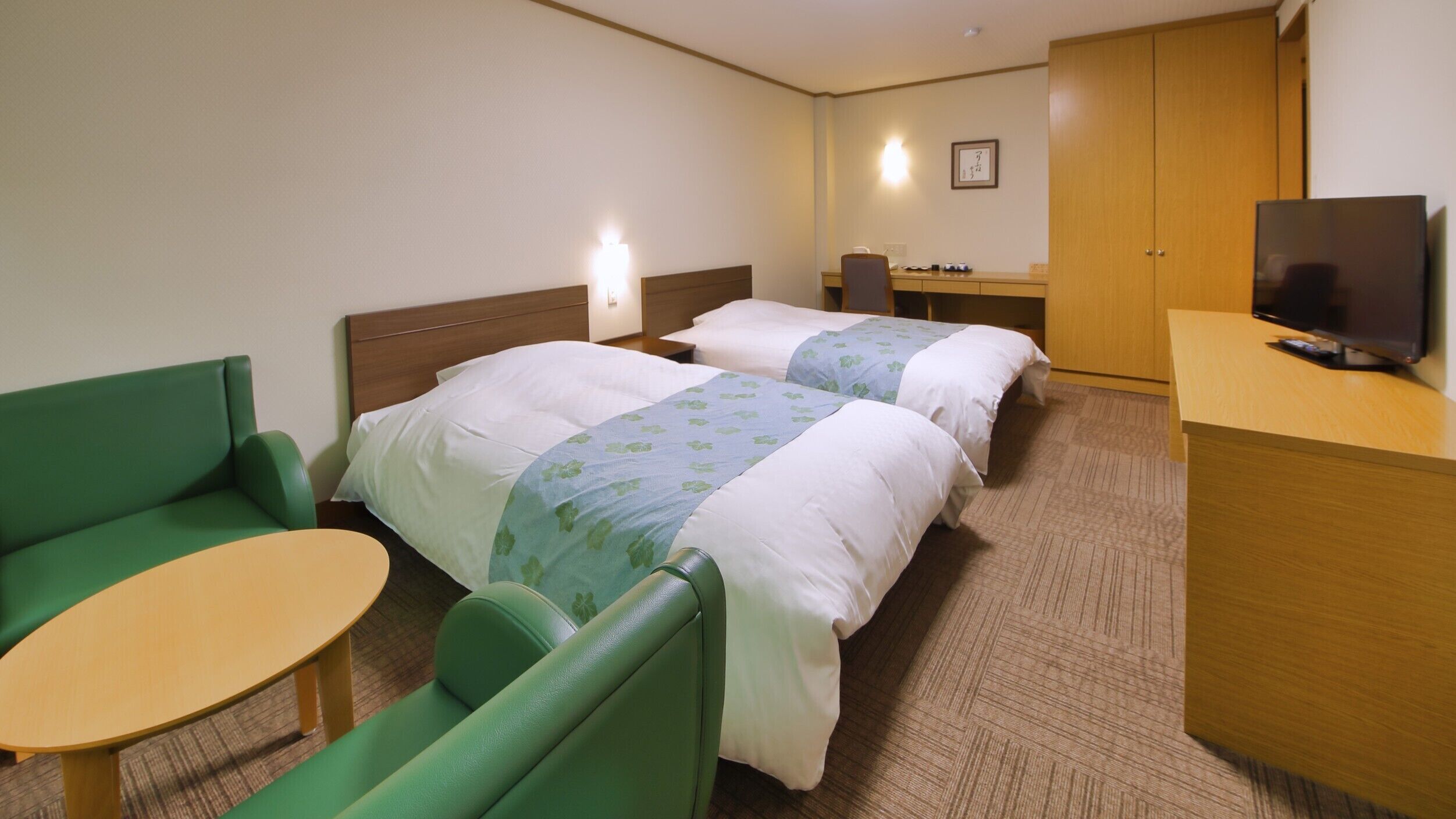 A hotel room with two beds, a green sofa, a small table, a TV, and a wooden wardrobe.