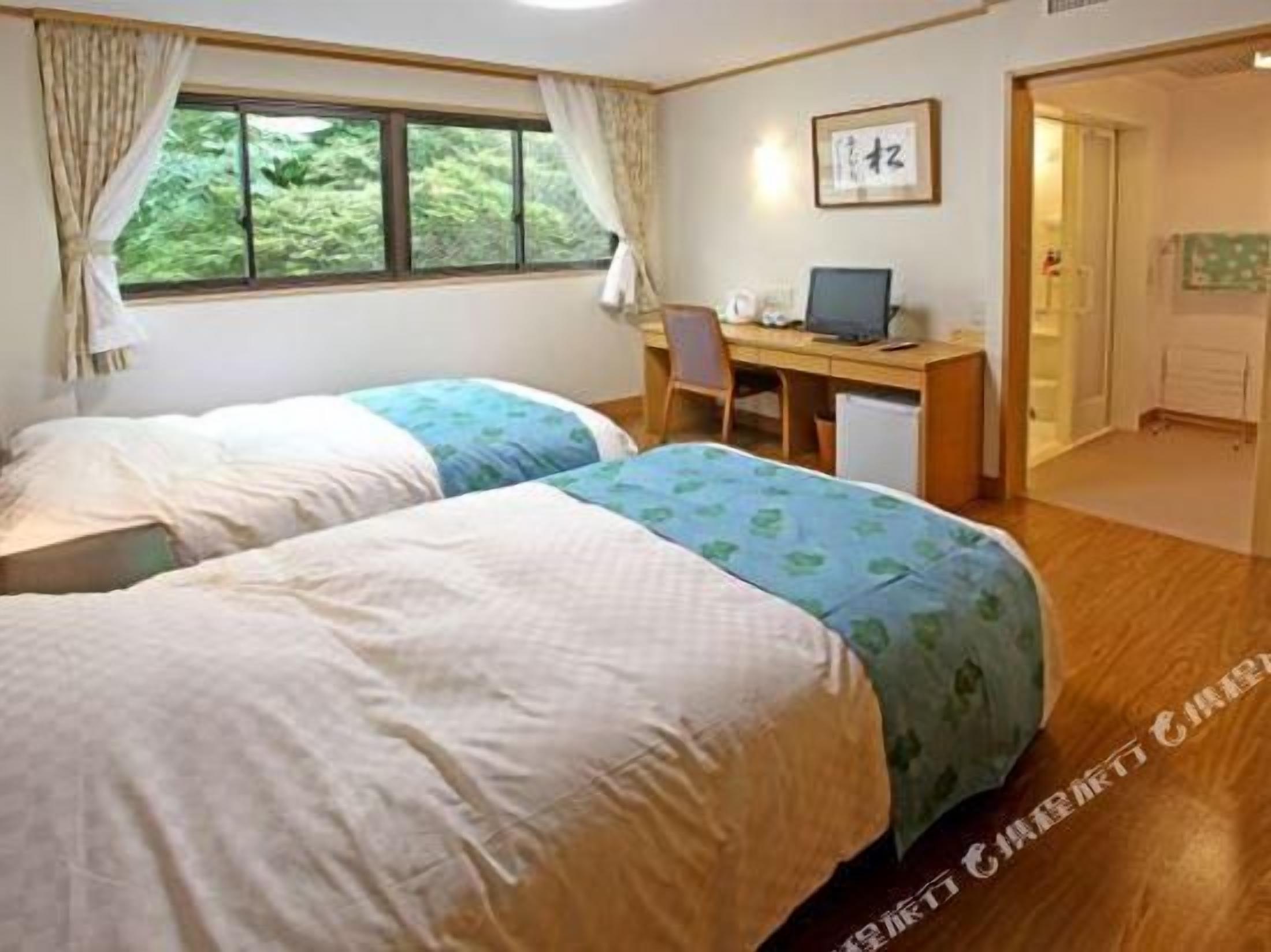A room with two beds, a desk with a computer, and a window with curtains.