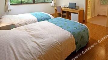 A room with two beds, a desk with a computer, and a window with curtains.