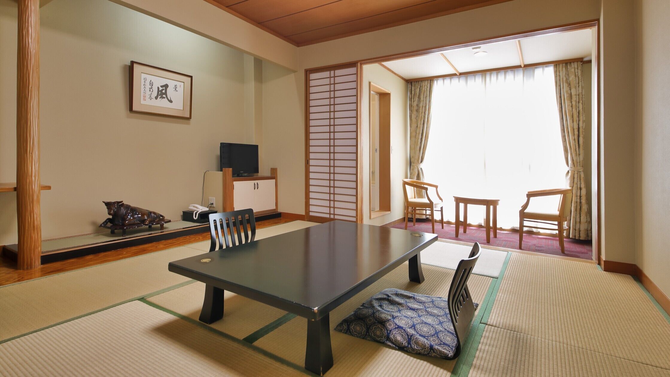 A traditional Japanese room with tatami flooring, a low table, chairs, a television, and a sliding door.