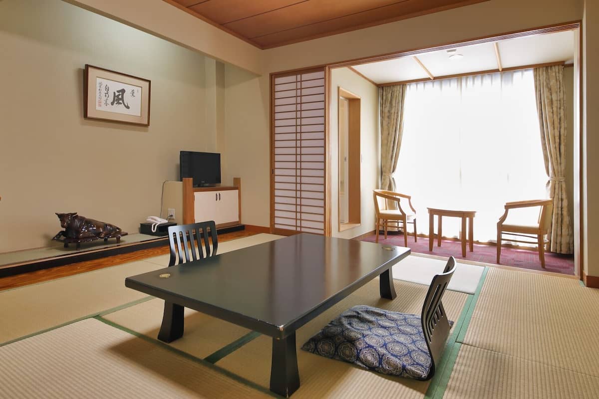 A traditional Japanese room with tatami flooring, a low table, chairs, a television, and a sliding door.