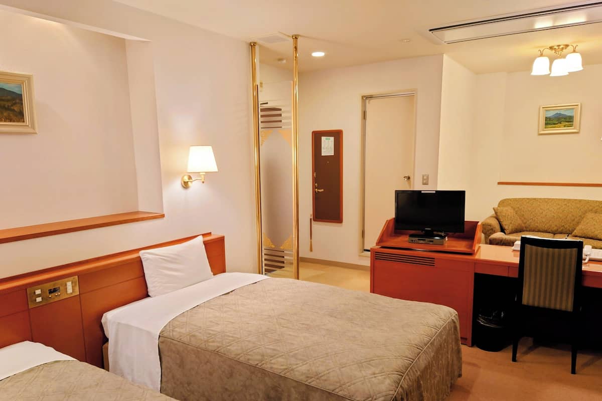 A hotel room with two beds, a desk with a television, a chair, and a mirror.