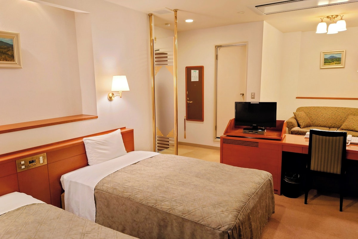 A hotel room with two beds, a desk with a television, a chair, and a mirror.