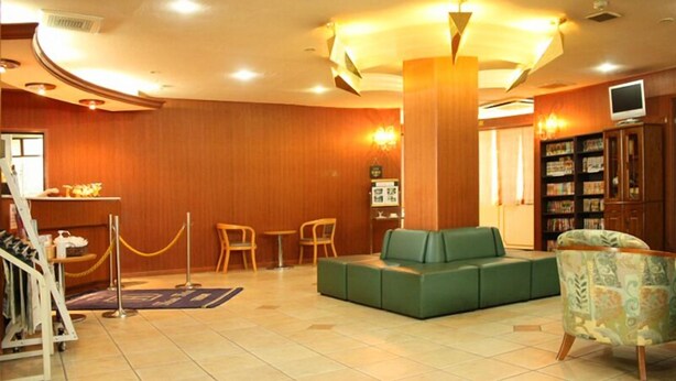 A lobby with a green sofa, wooden walls, a reception desk, and a television. - Heisei Hotel (Chikusei)