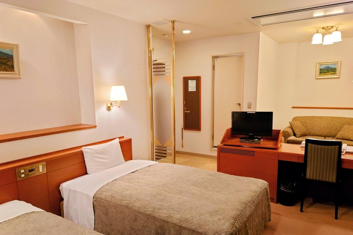 A hotel room with two beds, a desk with a television, a chair, and a sofa.