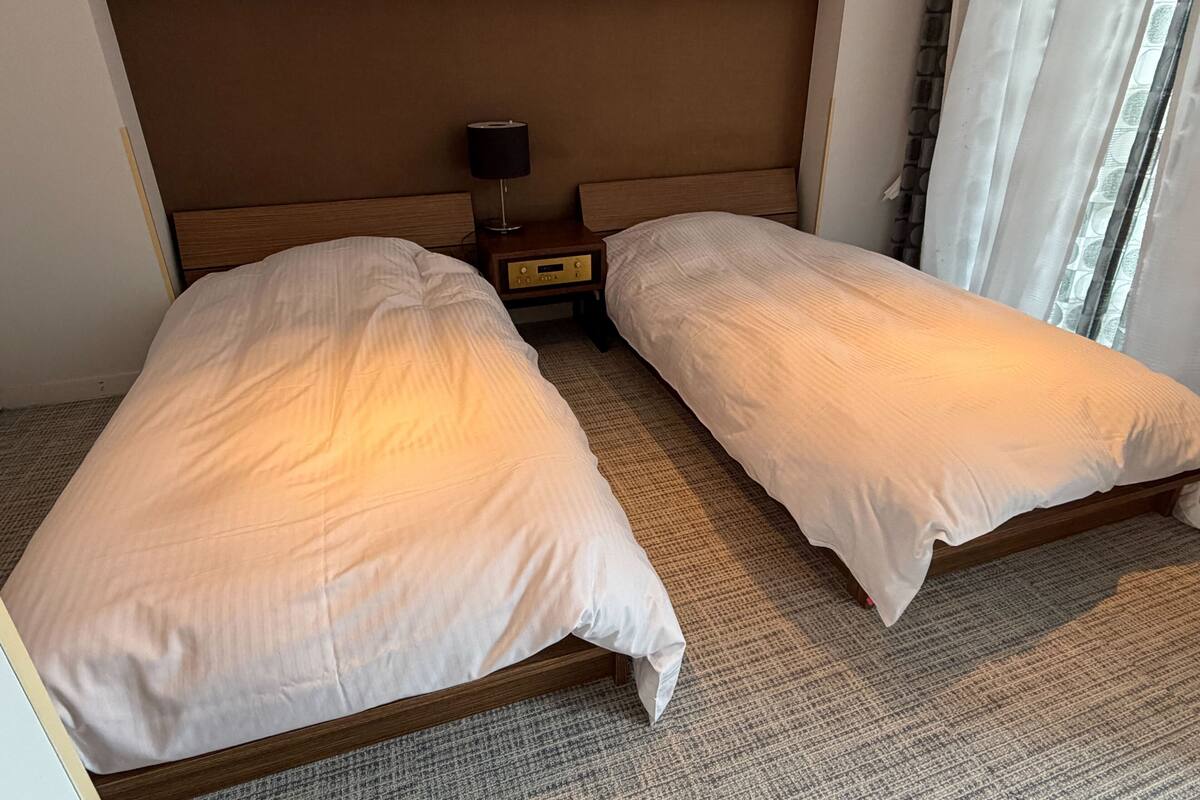 A hotel room with two single beds, a nightstand with a lamp, and a window with curtains.
