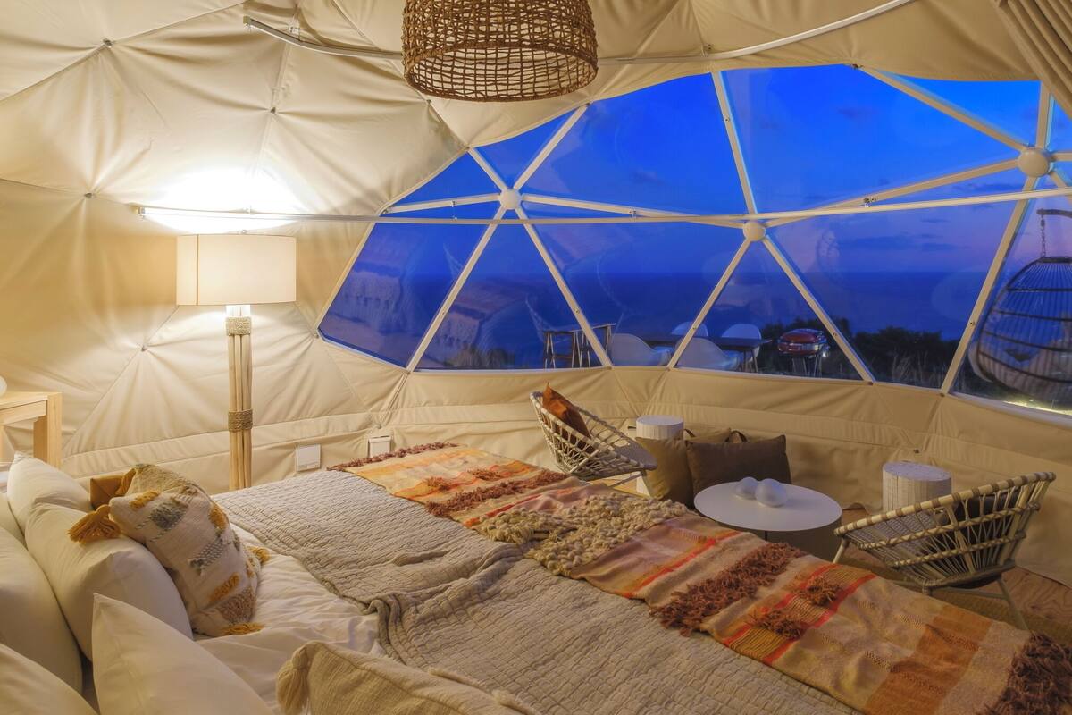 A cozy tented accommodation with a bed, pillows, a small table, and a chair.