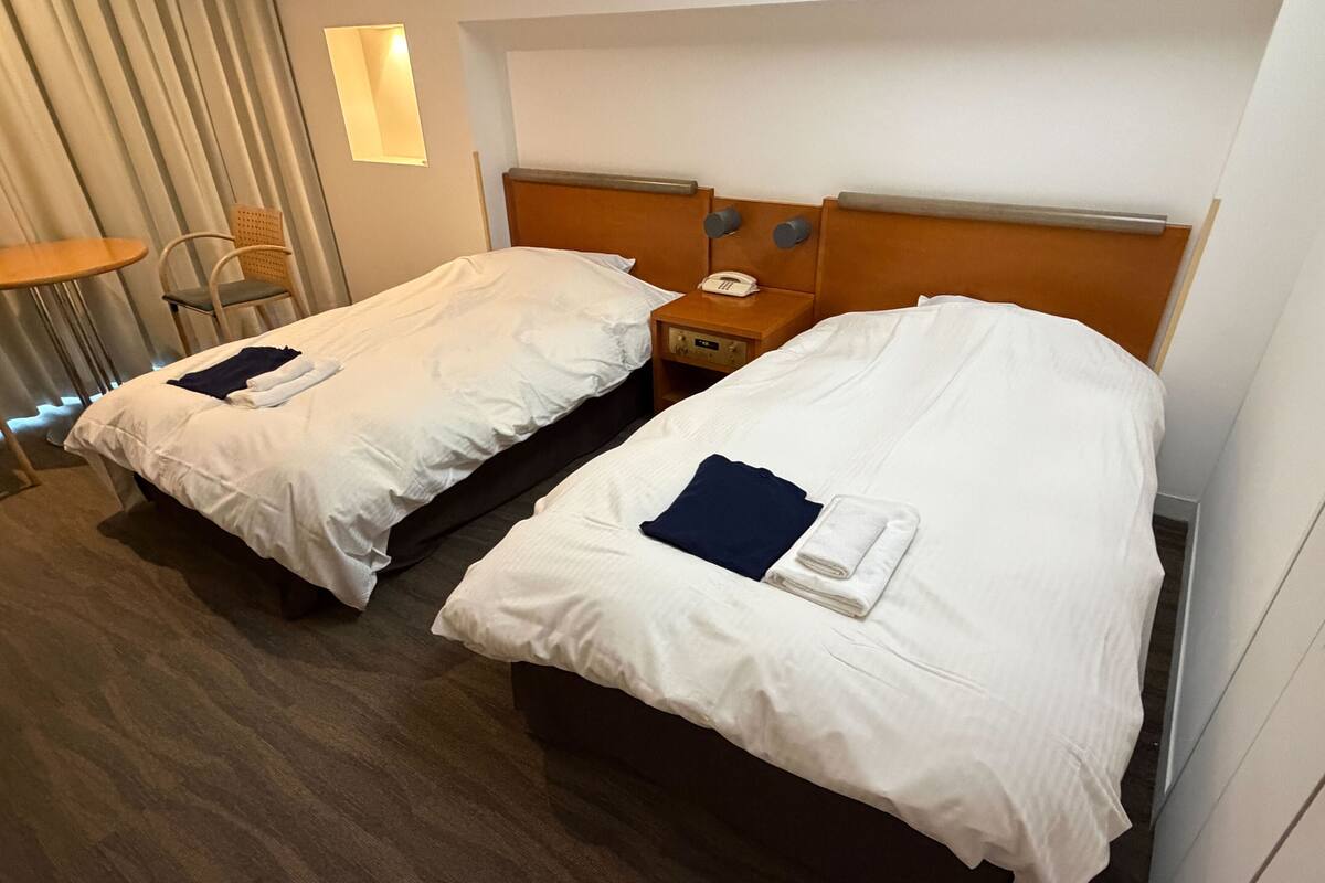 Two twin beds with white linens, a bedside table with a telephone, and a chair.