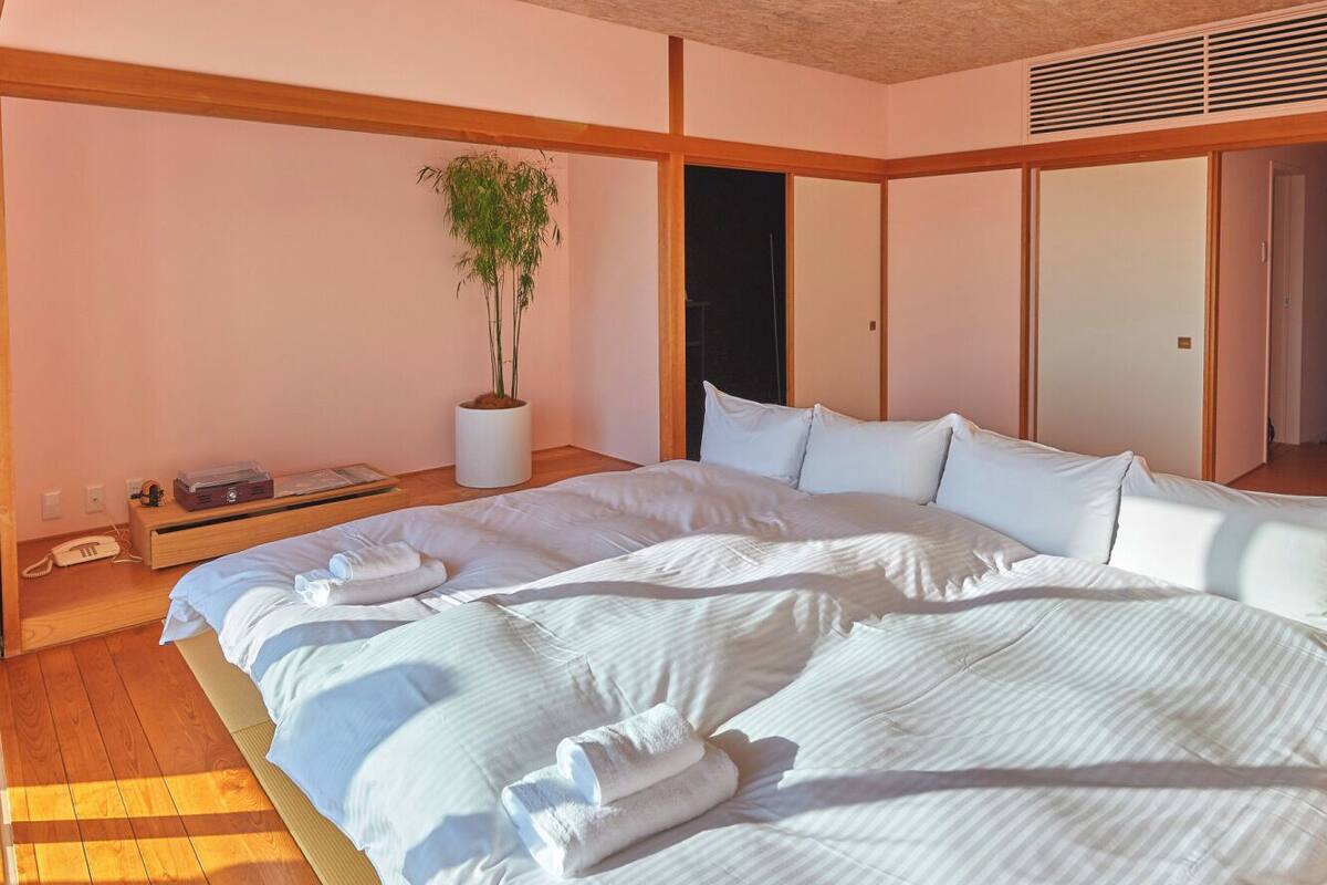 A bedroom with a large bed, a bedside table with a lamp, and a potted plant.