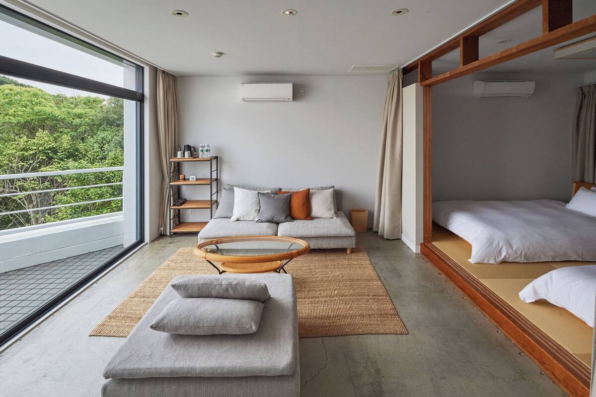 A modern bedroom with a sofa, a daybed, a wicker coffee table, and a small shelf unit.