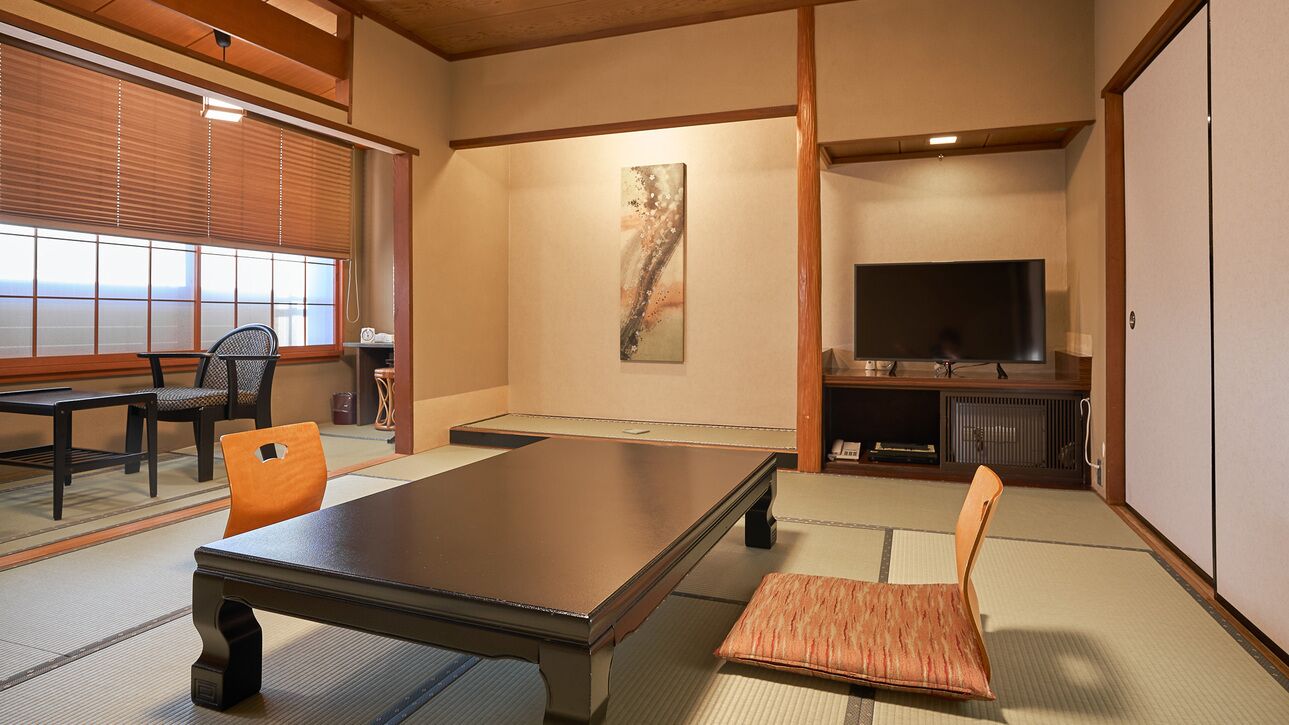 A traditional Japanese-style room with tatami flooring, a low table, a cushioned chair, a television, and a sliding door.