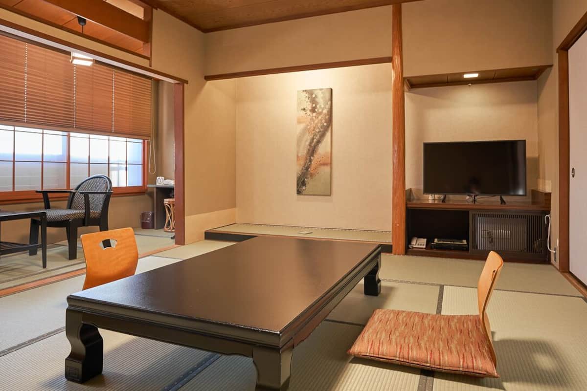 A traditional Japanese-style room with tatami flooring, a low table, a cushioned chair, a television, and a sliding door.