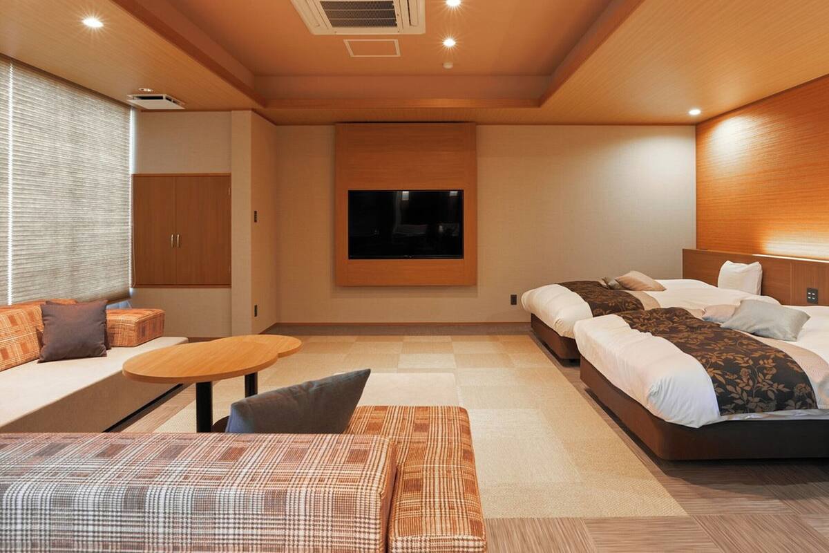 A modern hotel room with a sofa, a bed, a TV, and a small table.