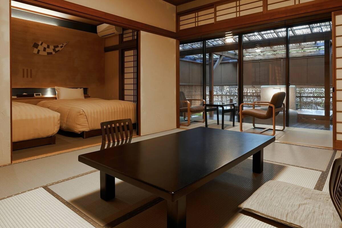 A traditional Japanese-style room with tatami flooring, a low table, and a bed with a futon.