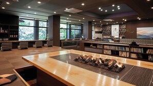 A modern bar area with a wooden counter, a fire feature, and bookshelves. - Itoyanagi Koyado Yuwa (Fuefuki)