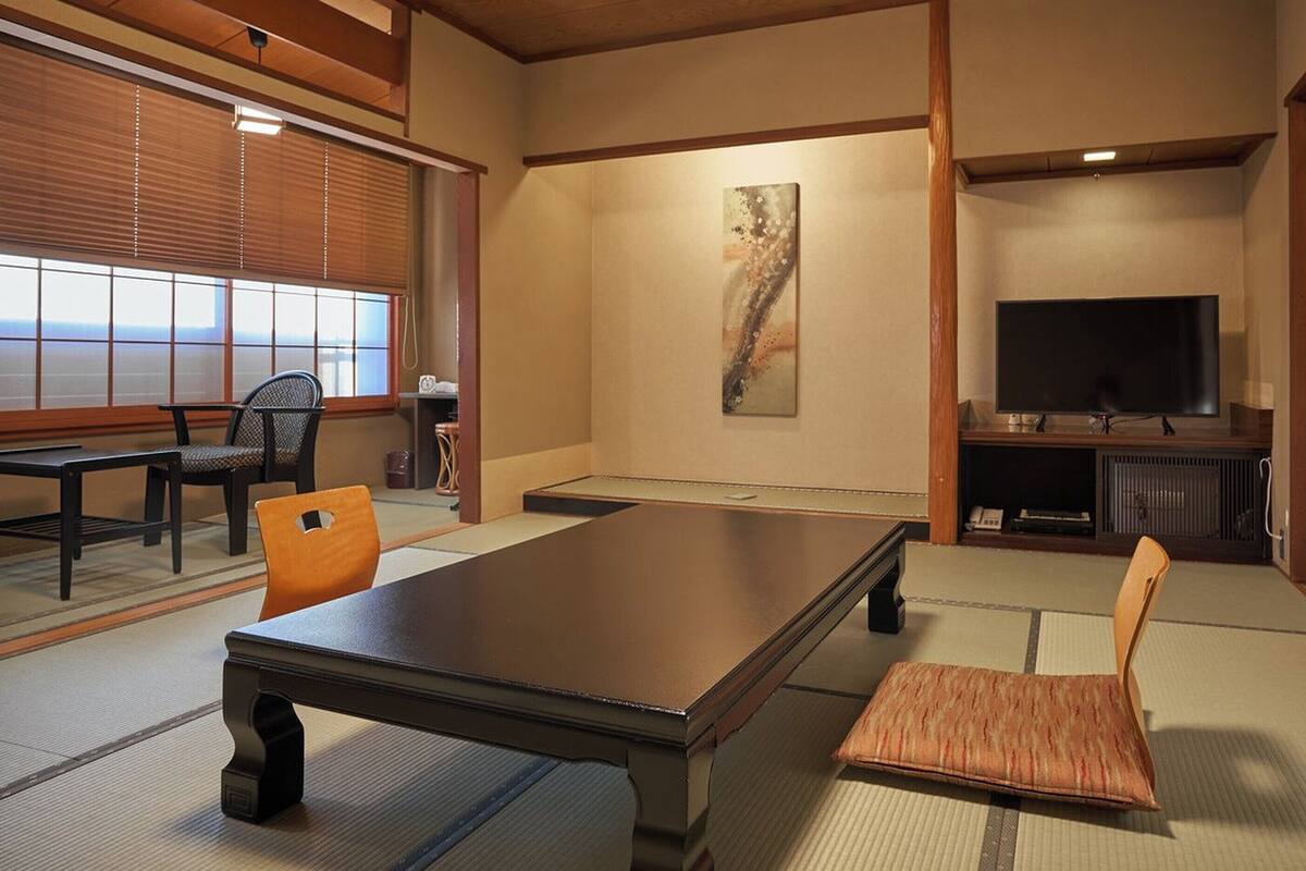 A traditional Japanese-style room with tatami flooring, a low table, a sofa, and a television.