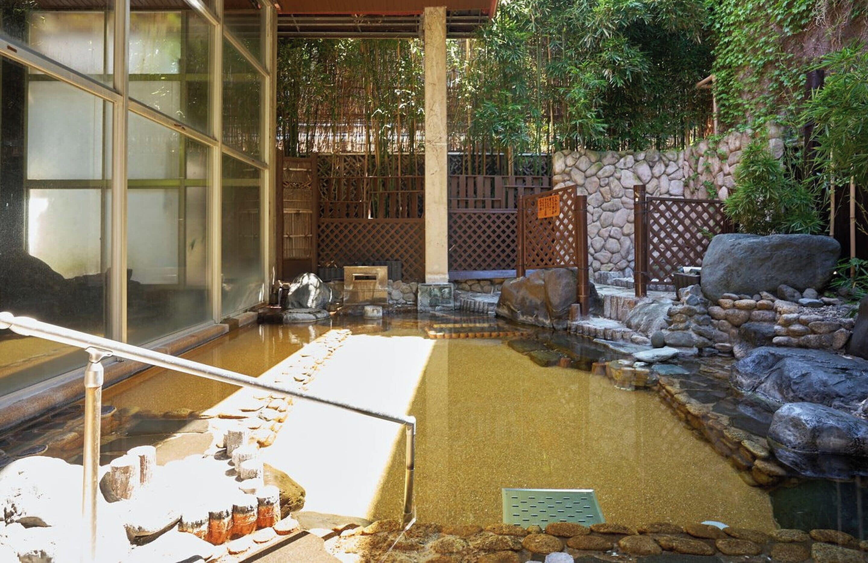 A traditional Japanese onsen with a stone bath, wooden fence, and bamboo plants.
