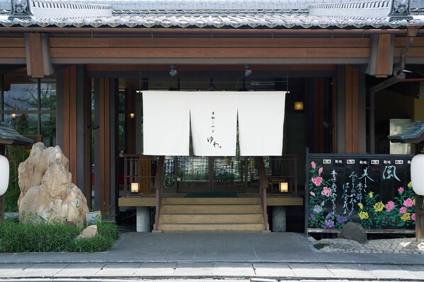 A traditional Japanese building entrance with a wooden structure, a stone rock, and a signboard with floral designs. - Itoyanagi Koyado Yuwa (Fuefuki)