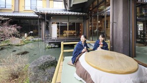 A traditional Japanese ryokan with tatami mat flooring, a wooden platform overlooking a koi pond, and a view of the building's interior through large glass windows. - Itoyanagi Koyado Yuwa (Fuefuki)