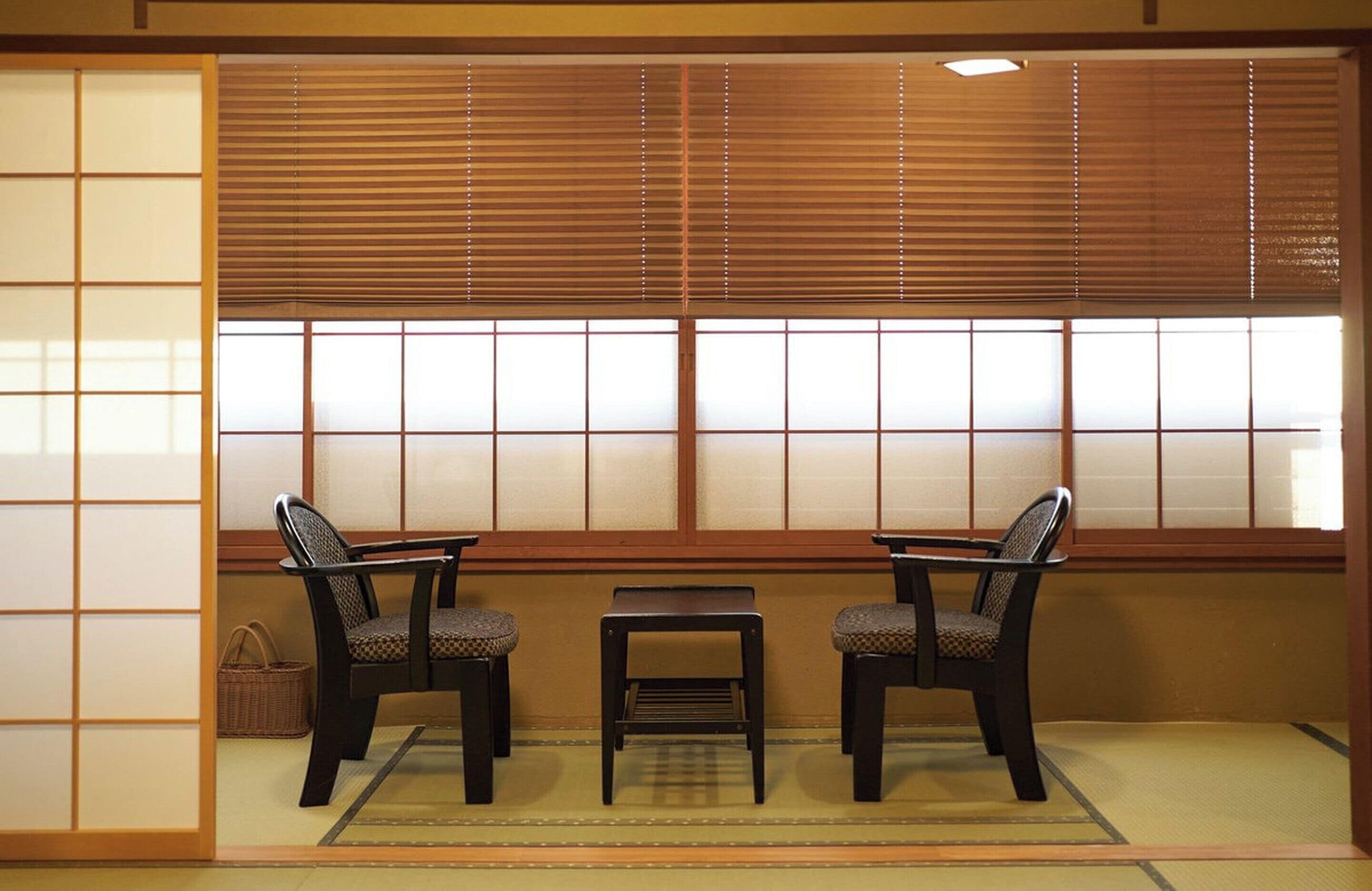 A traditional Japanese room with tatami flooring, a low table, two chairs, and shoji screens.