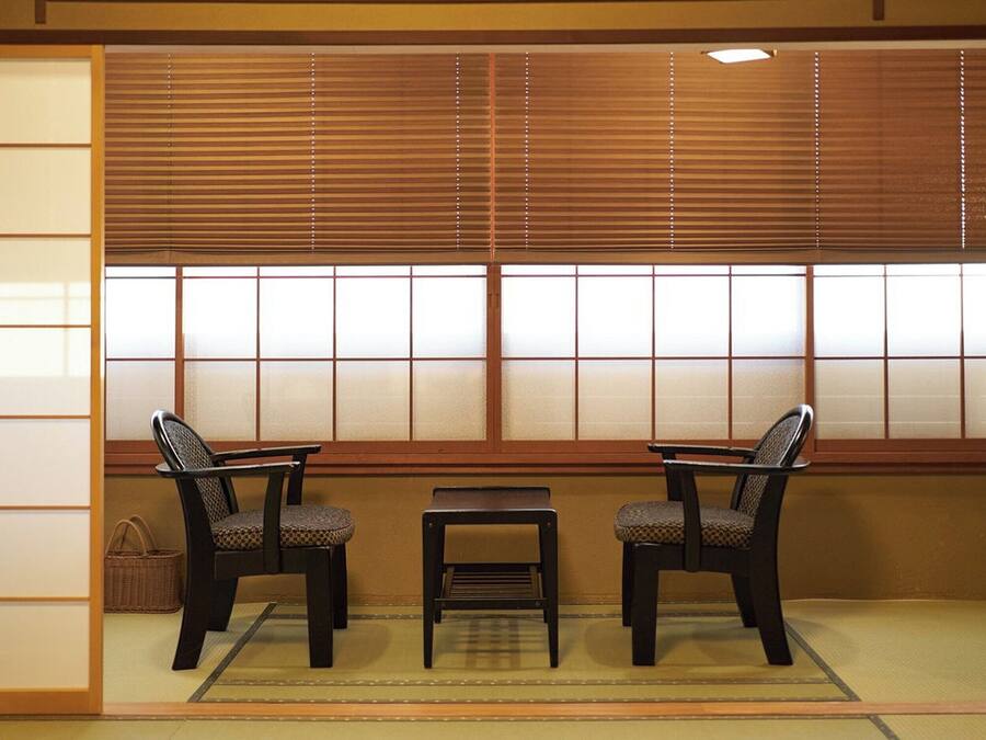 A traditional Japanese room with tatami flooring, a low table, two chairs, and shoji screens.