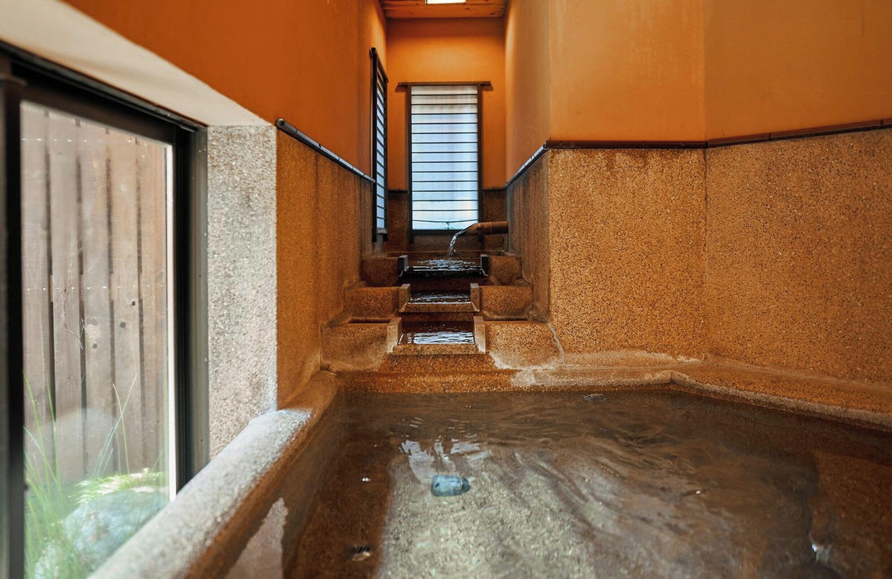 A narrow corridor with a water feature at the bottom, leading to a window with blinds.