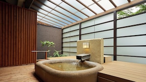 A hot tub in a modern spa area with a wooden floor, a stone wall, and a glass partition. - Itoyanagi Koyado Yuwa (Fuefuki)