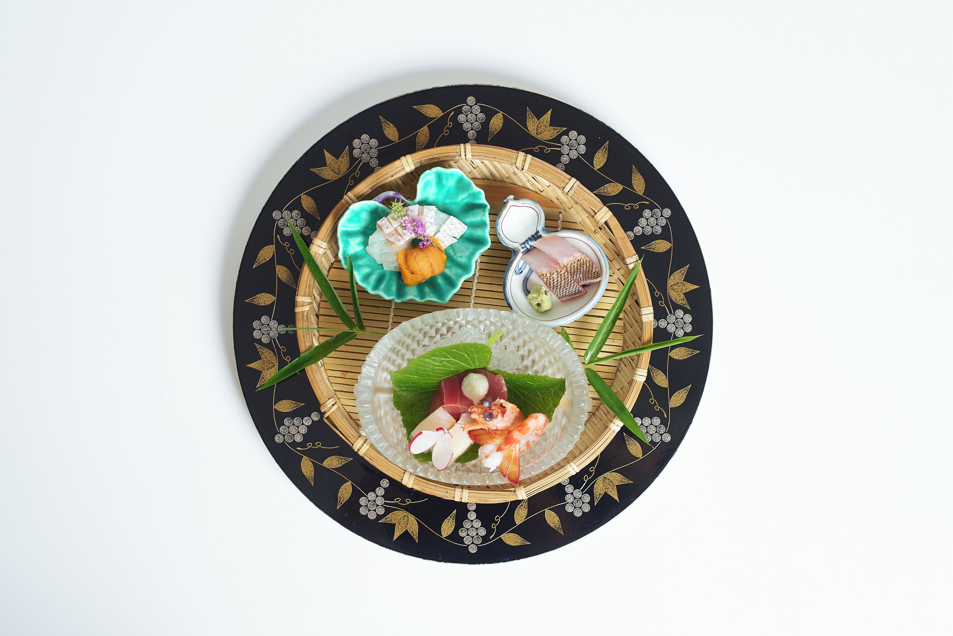 Una mesa redonda con un diseño decorativo negro y dorado, una hoja verde y un pequeño plato con alimentos.