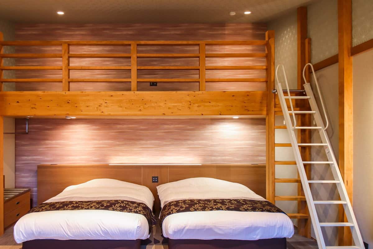 A bunk bed room with a wooden ladder, a small bedside table, and a wall-mounted light.