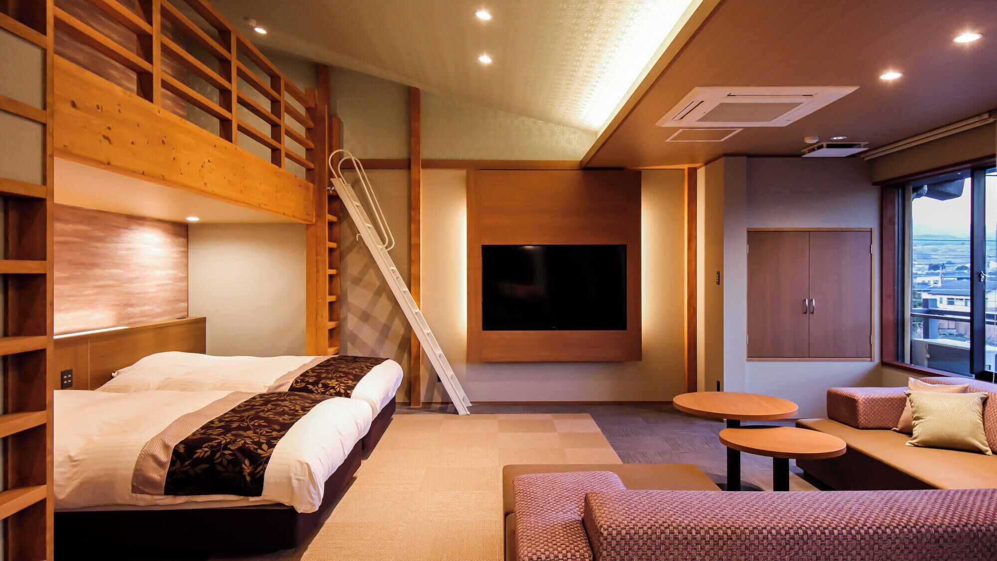 A modern hotel room with a bunk bed, a TV mounted on the wall, a sofa, and a small table.