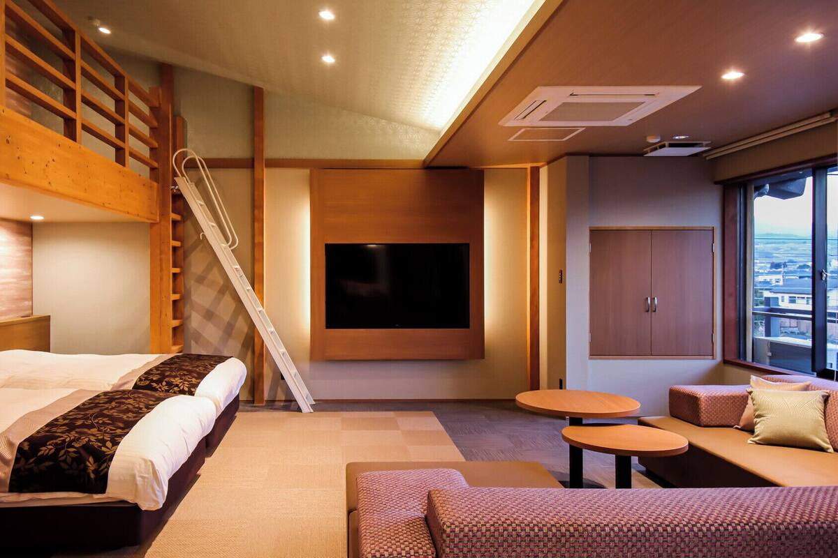 A modern hotel room with a bunk bed, a TV mounted on the wall, a sofa, and a small table.