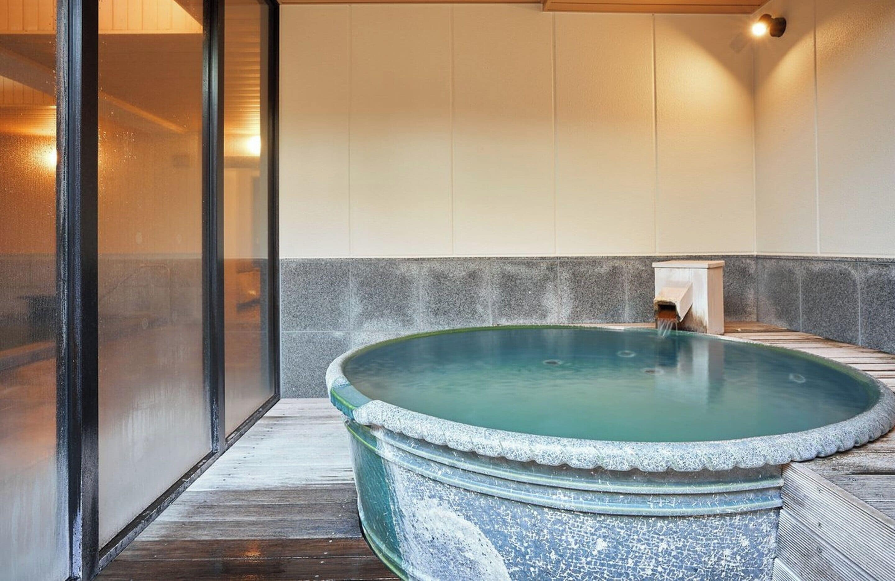 A spa area with a large circular hot tub, a wooden bench, and a small waterfall feature.