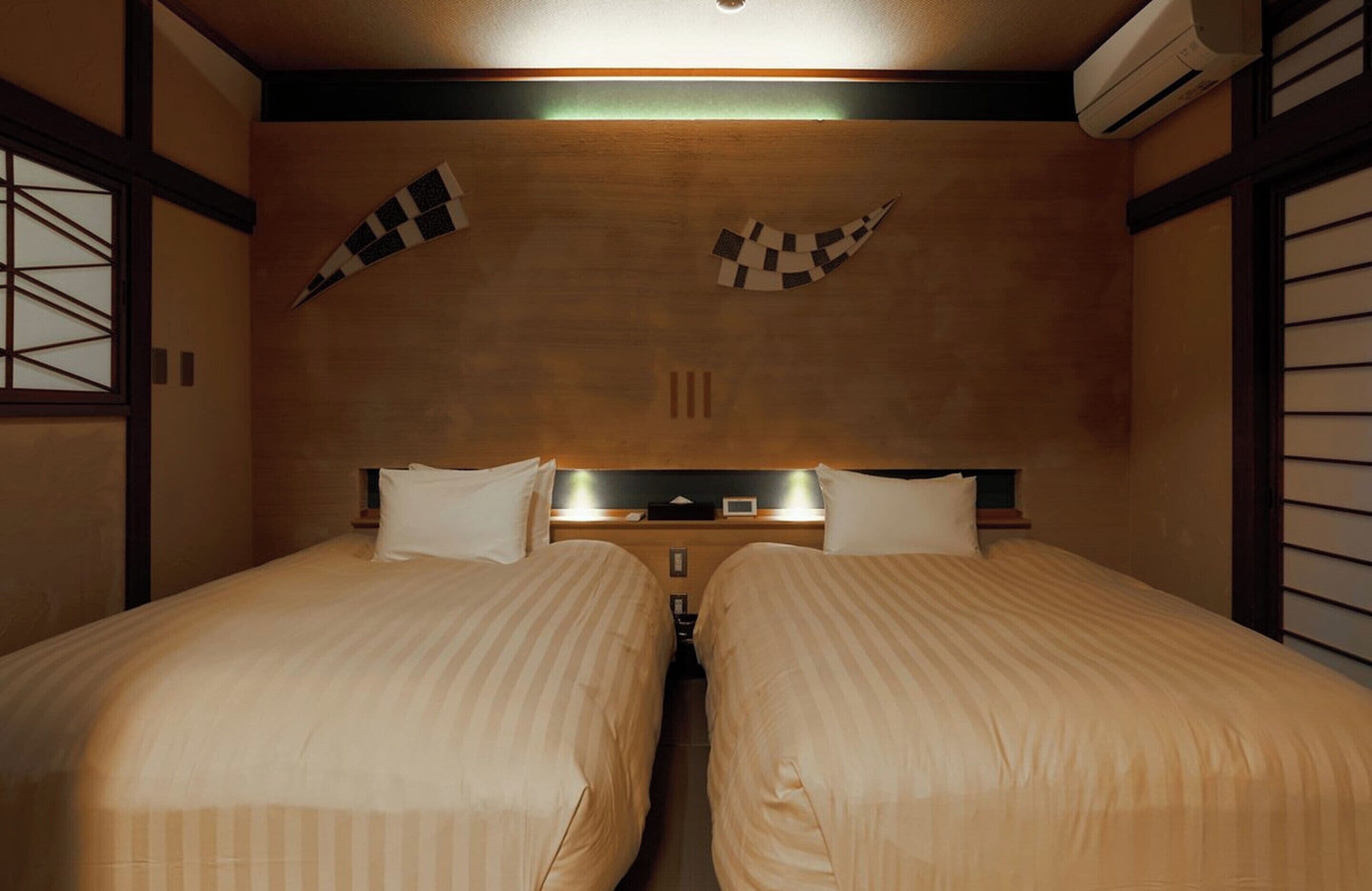 Quarto de hotel com duas camas, cabeceira de madeira, decorações na parede em padrão xadrez e um aparelho de ar condicionado.