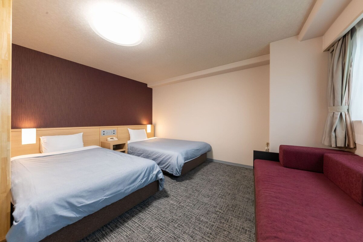 A hotel room with two beds, a red sofa, a wooden headboard, and a carpeted floor.