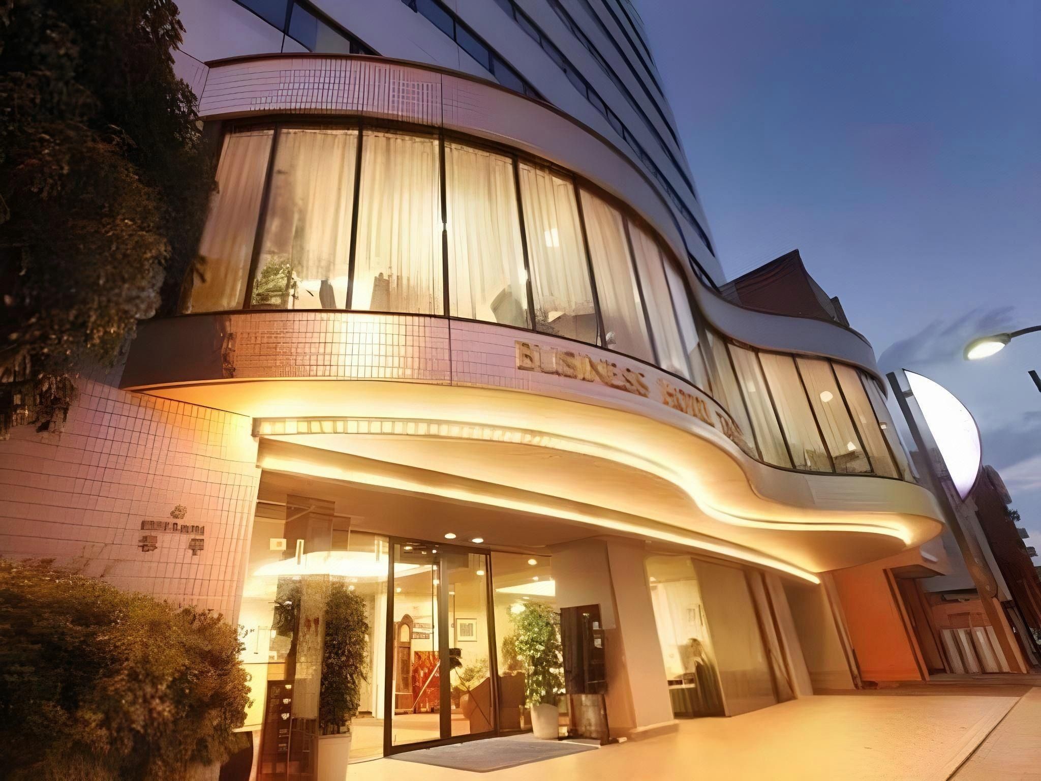 Un edificio moderno con fachada curva, grandes ventanales de vidrio y un letrero que dice 'BUSINESS HOTEL'.