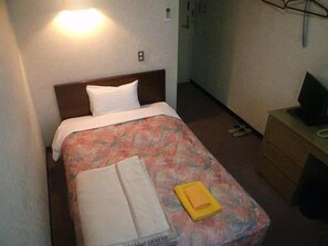 A small, neatly made bed with a floral bedspread, a white pillow, and a folded towel on the foot of the bed. - Hotel Nakajima (Saku)