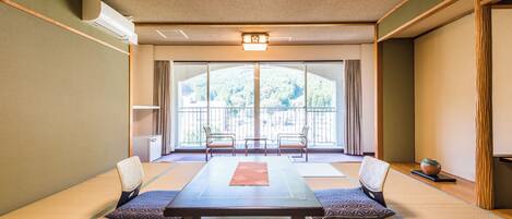 A tatami mat room with a low table, two chairs, and a view of a forest through large windows.