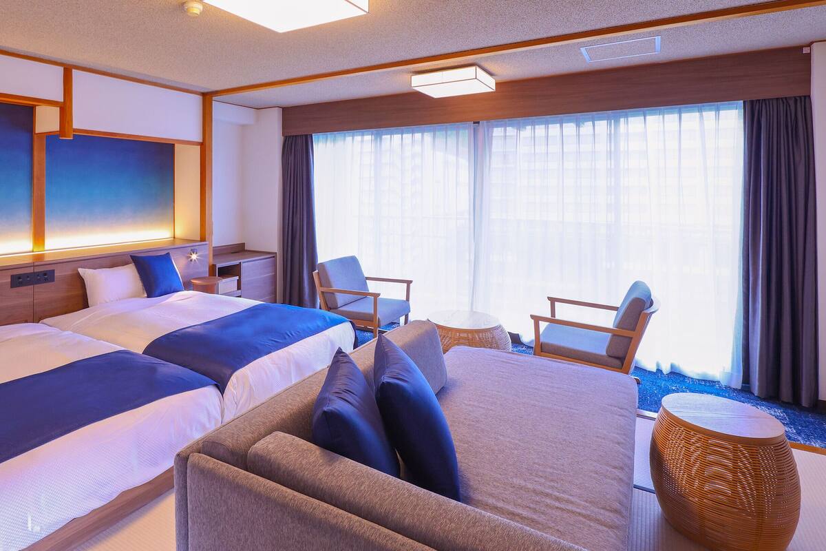 Ett modernt hotellrum med två stora sängar, en soffa, ett litet bord och en stol.