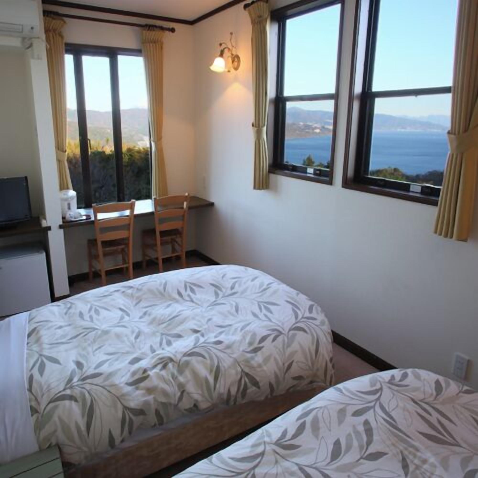 A bedroom with a bed, a desk, and a chair. There are two windows with curtains.