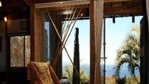 A wooden interior with a rocking chair, a view of palm trees, and a large window. - Ito Onsen Ocean View Villa Jaiz (Ito)