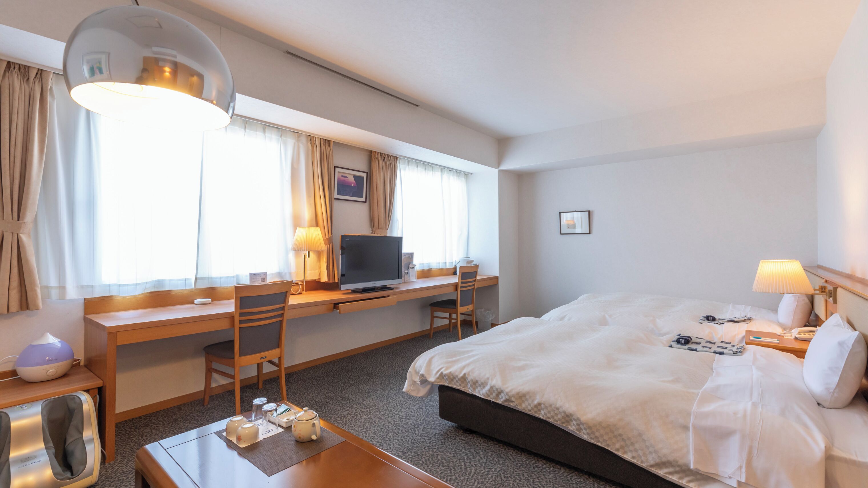 Habitación de hotel con cama, escritorio, silla, televisor, lámpara y sillón de masaje.
