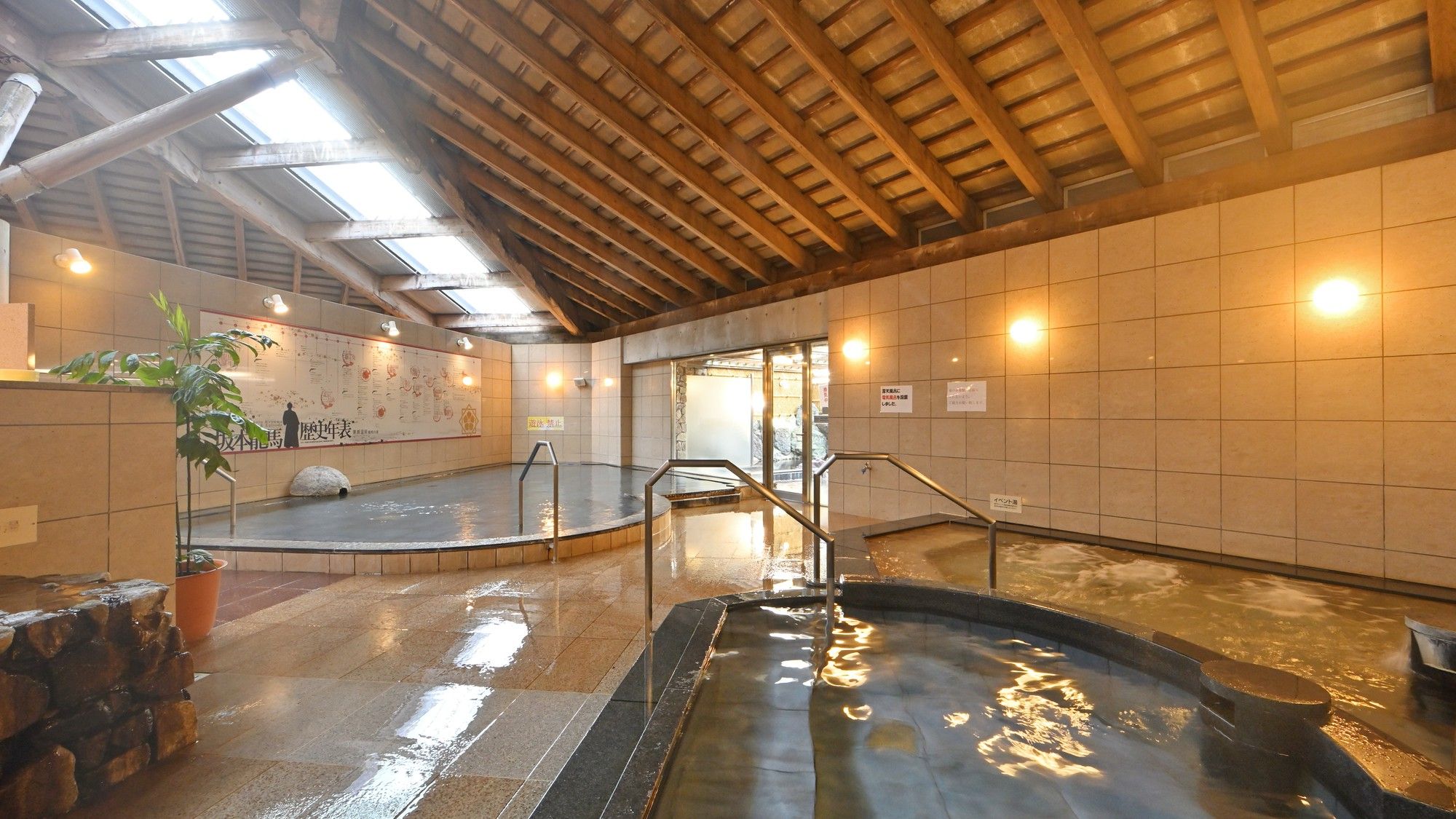Ein Thermalbadbereich mit gefliesten Wänden, Holzbalken und einer Steinwand.